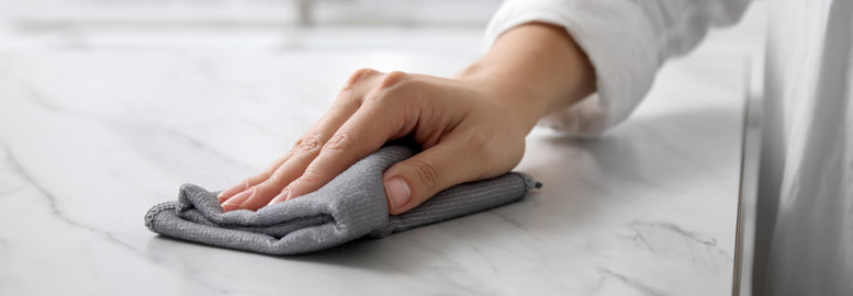 Home cleaning Hand som torkar en marmorbänk med en grå trasa.